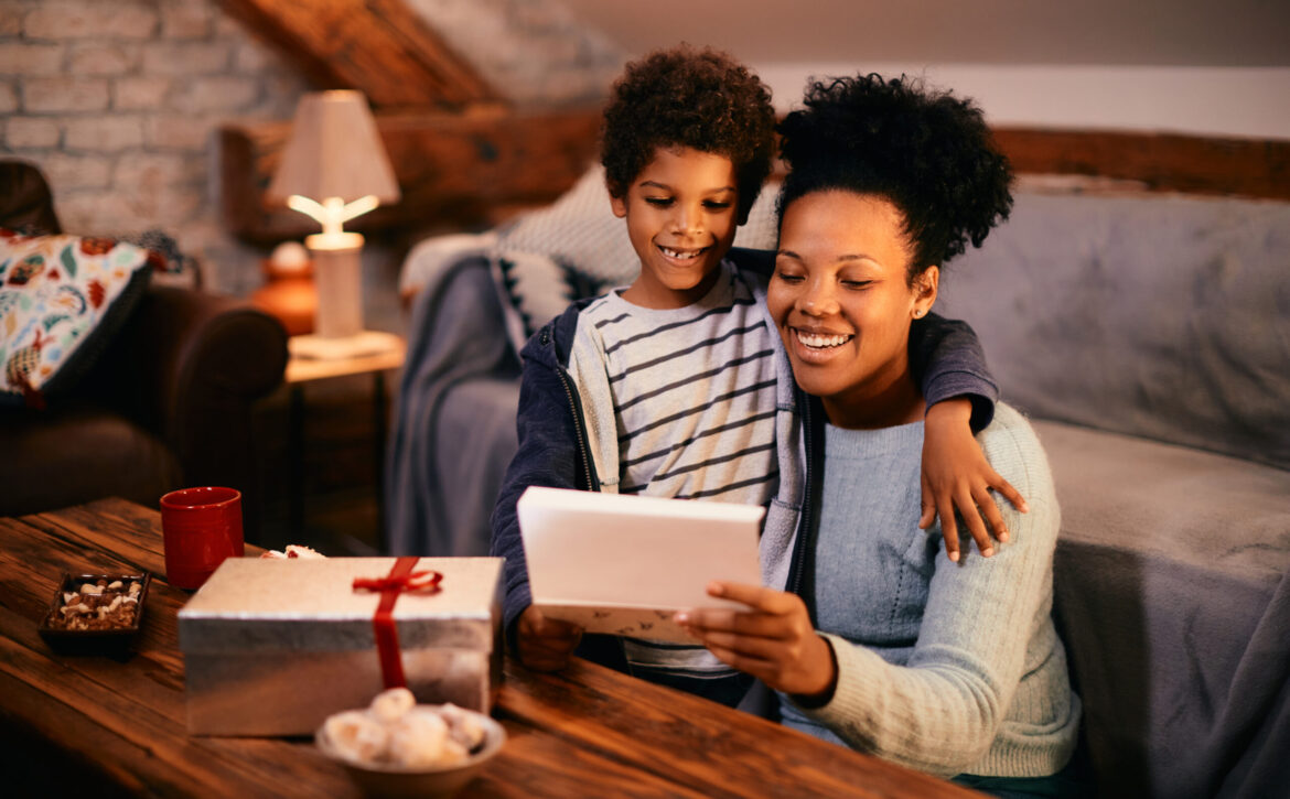 Happy black mother receiving gift and greeting card from her son on Mother's day.